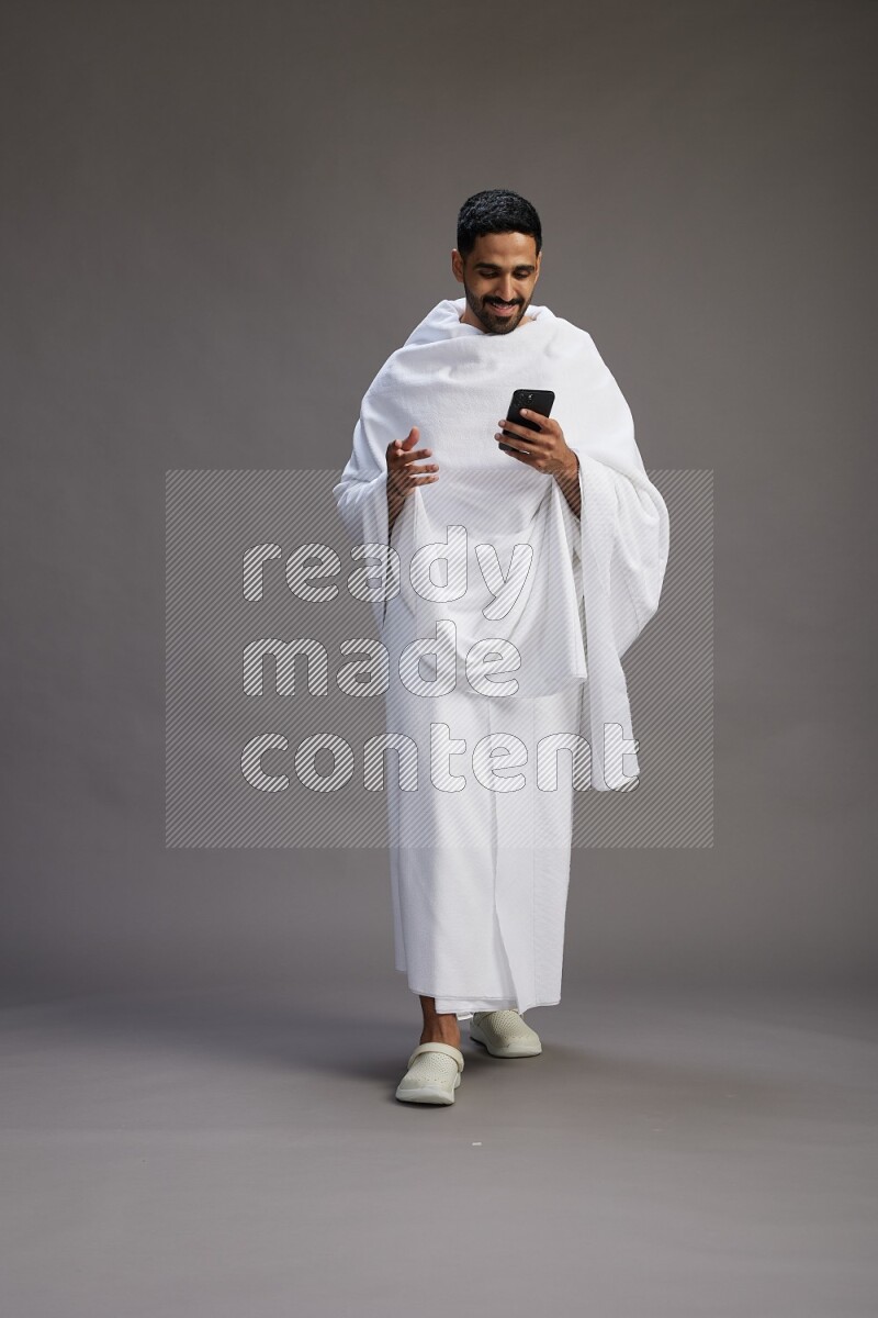 A man wearing Ehram Standing texting on phone on gray background