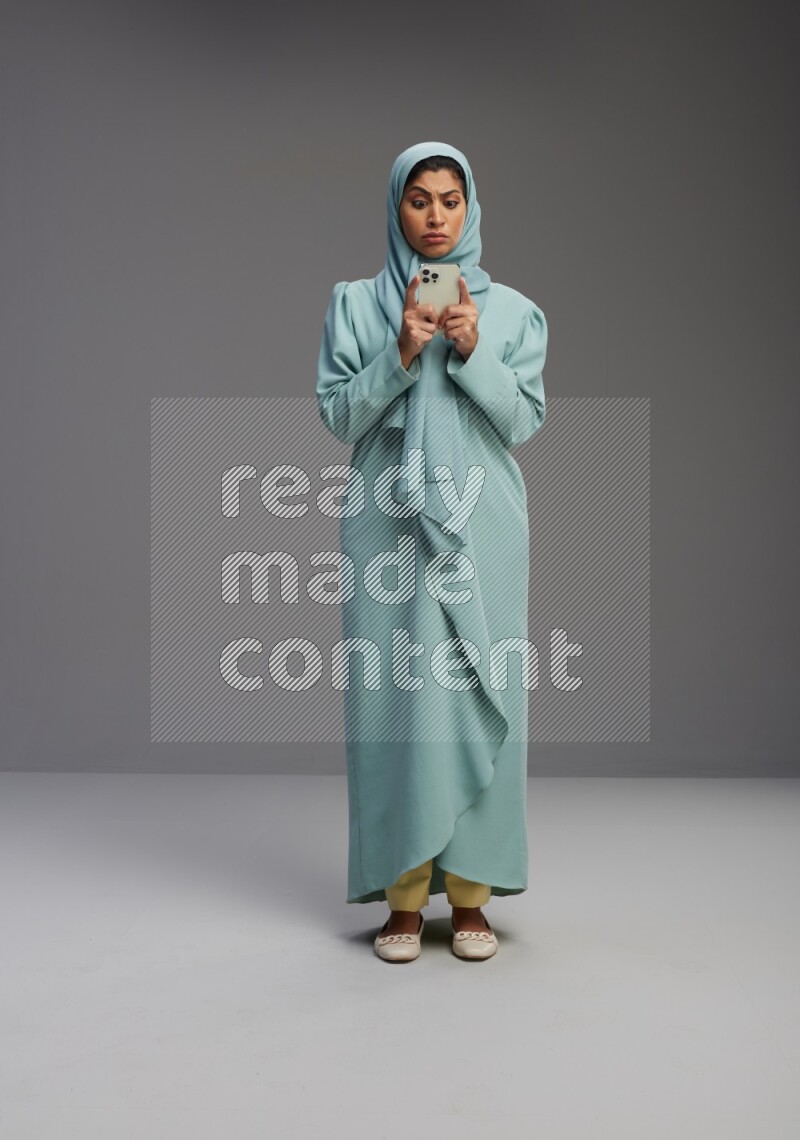 Saudi Woman wearing Abaya standing texting on phone on Gray background