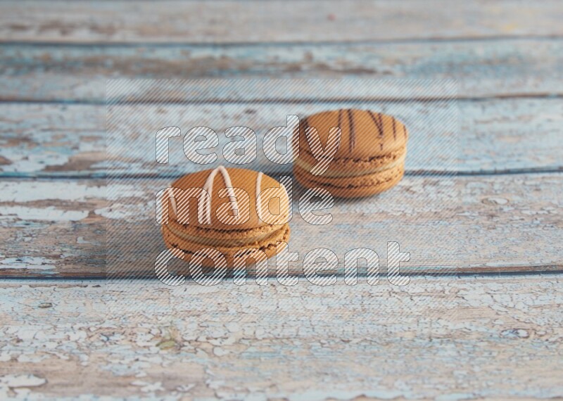 45º Shot of of two assorted Brown Irish Cream, and light brown Almond Cream macarons next to each other on light blue background