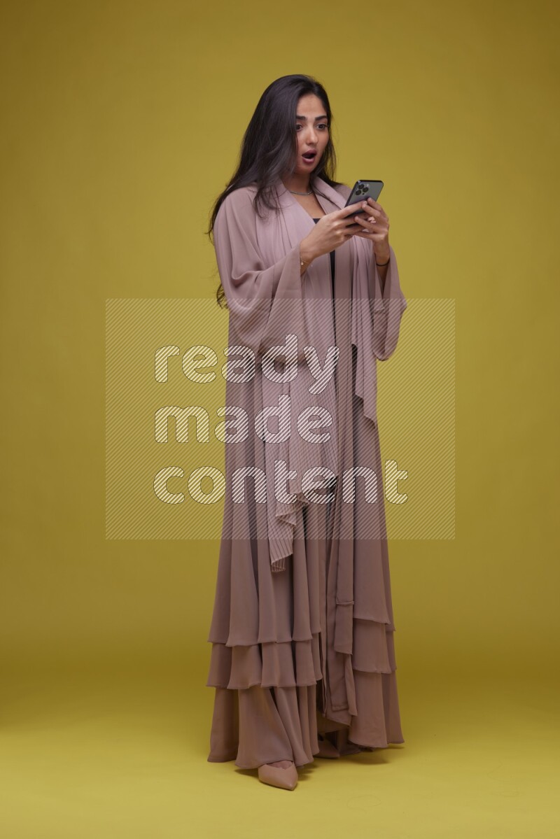 A woman Texting on a Yellow Background wearing Brown Abaya
