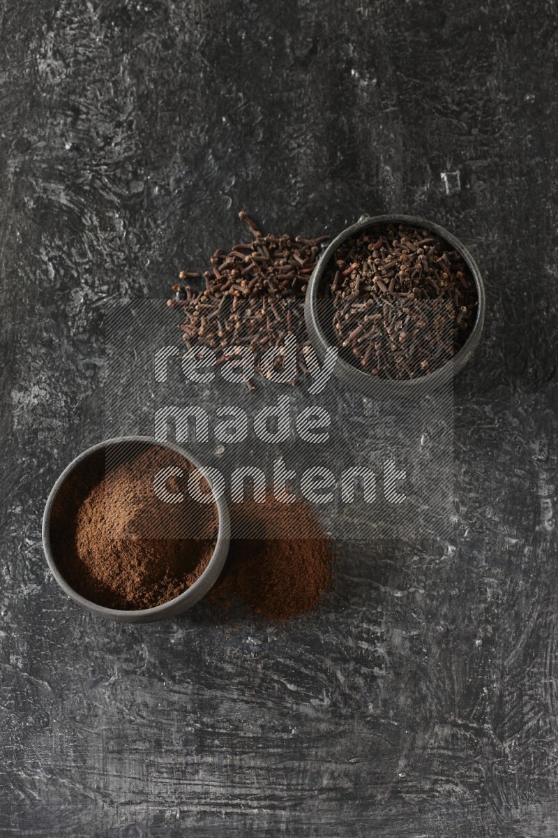 وعاءين من الفخار الأسود أحدهما ممتلئي بحبوب القرنفل والآخر ممتلئ ببودرة القرنفل على خلفية سوداء