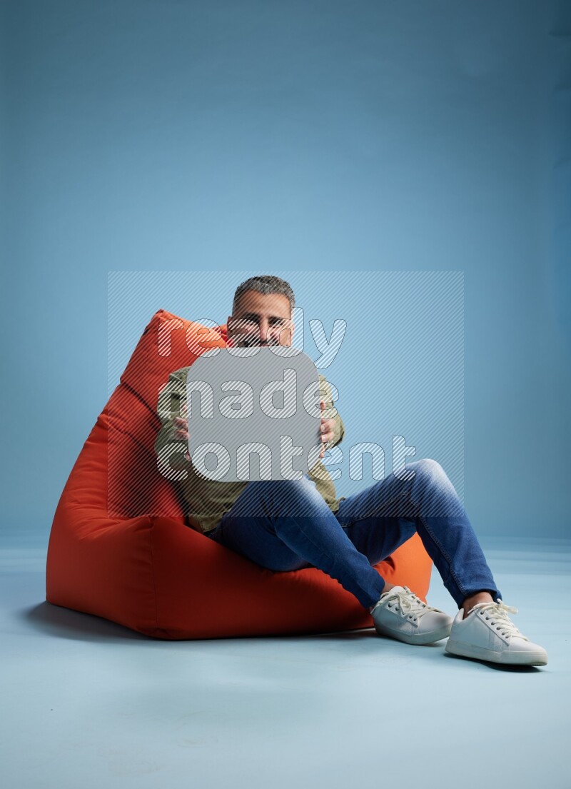 A man sitting on a orange beanbag and holding social media sign