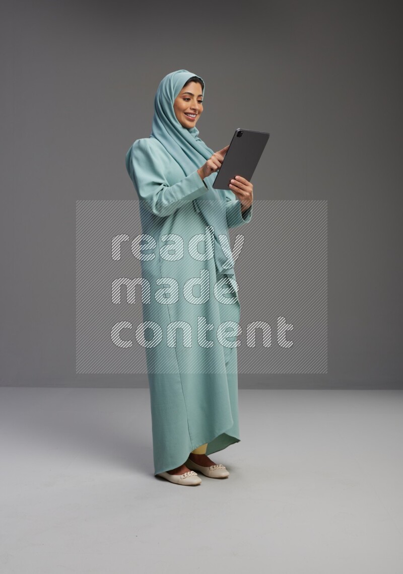 Saudi Woman wearing Abaya standing working on tablet on Gray background