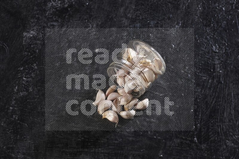 A glass jar full of garlic cloves flipped and the cloves came out on a textured black flooring