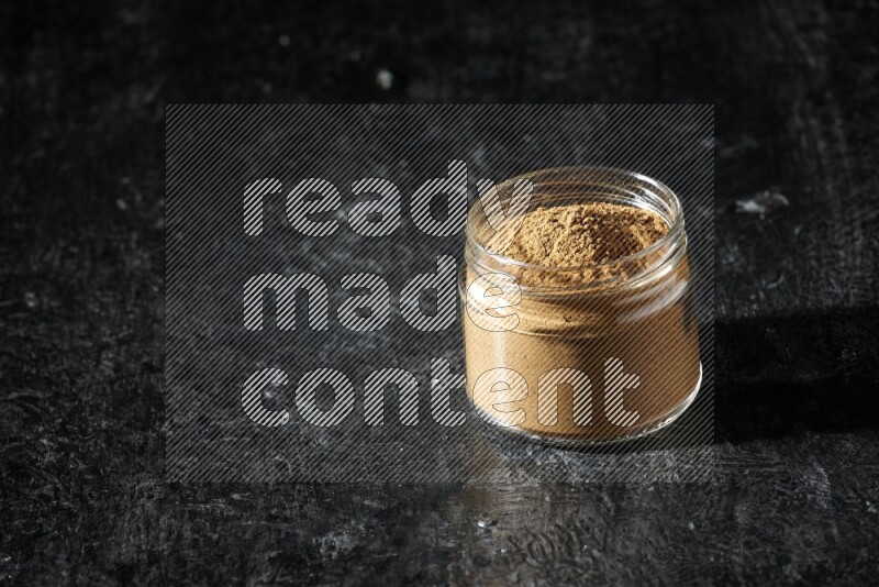 A glass jar full of allspice powder on a textured black flooring