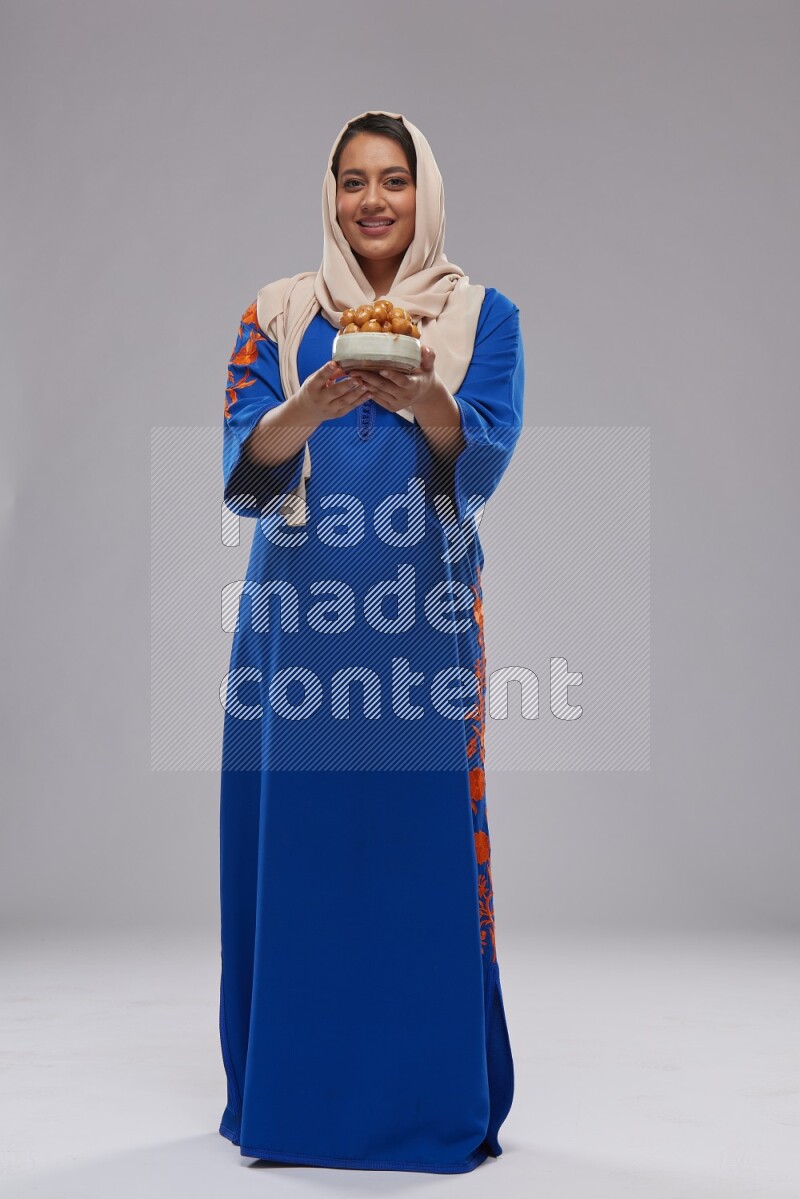 A Saudi woman standing wearing Jalabeya holding a plate of luqaimat