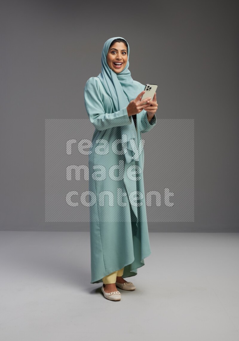 Saudi Woman wearing Abaya standing texting on phone on Gray background