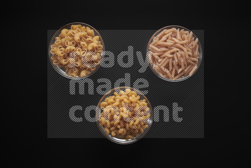 Different pasta types in glass bowls on black background