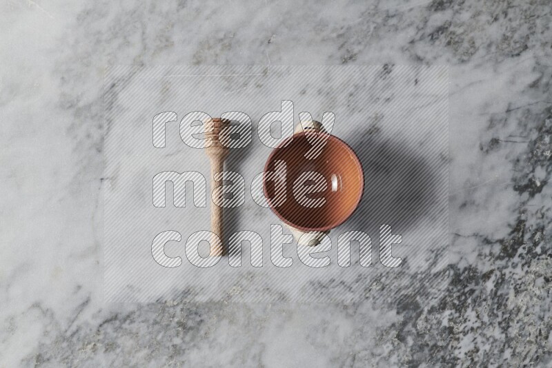 Brown pottery bowl with wooden honey dipper on the side on grey marble background