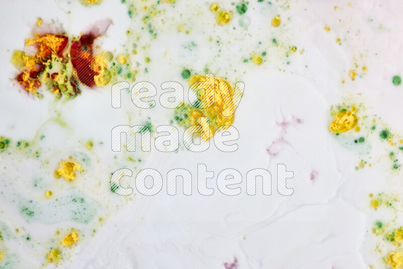 The image captures a splatter of yellow, red and green paint over a white backdrop