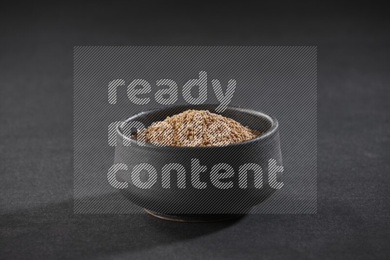 A black pottery bowl full of mustard seeds on black flooring