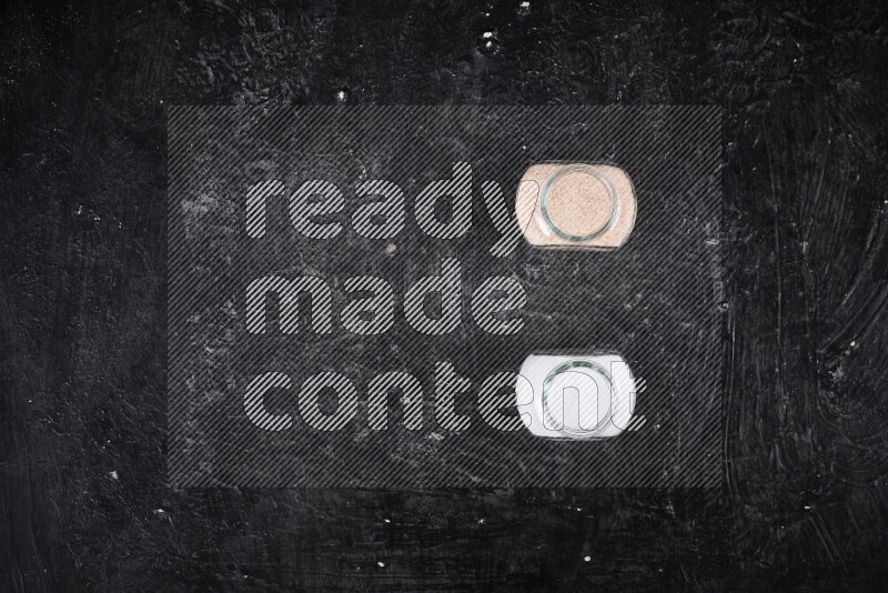 2 وعاء زجاجي احدهمها ممتلئ بملح الهيمالايا الناعم والأخر بملح الطعام على خلفية سوداء