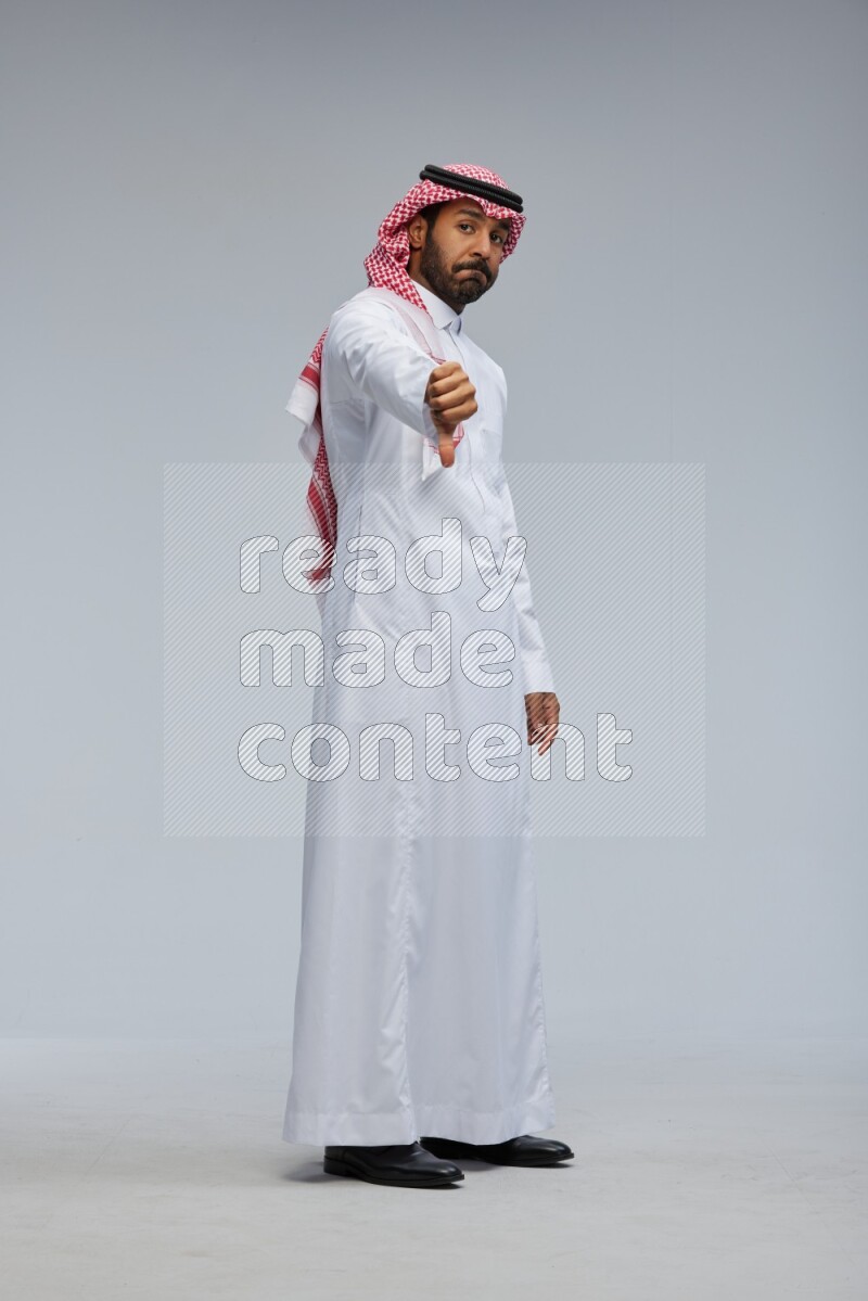 Saudi man Wearing Thob and shomag standing interacting with the camera on Gray background