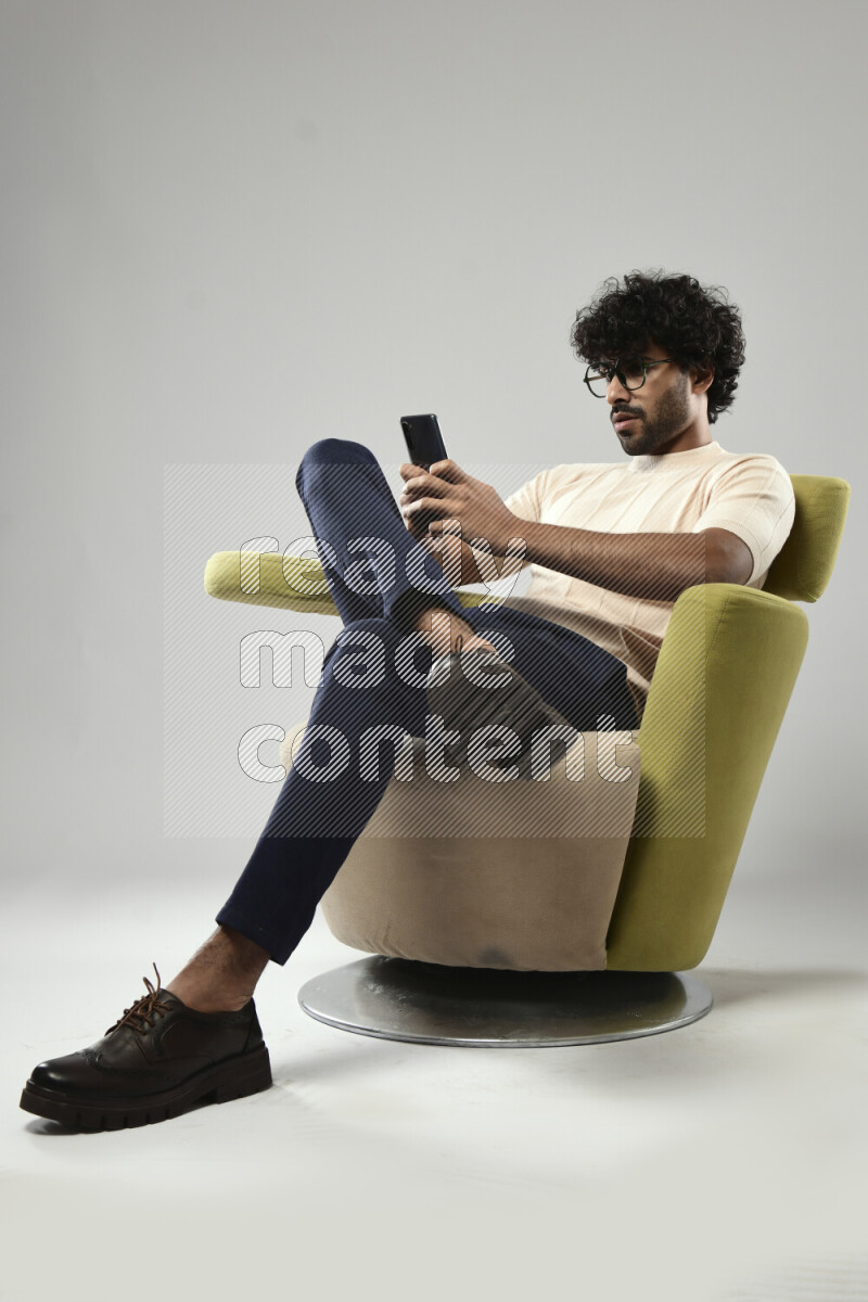 A man wearing casual sitting on a chair texting on the phone on white background