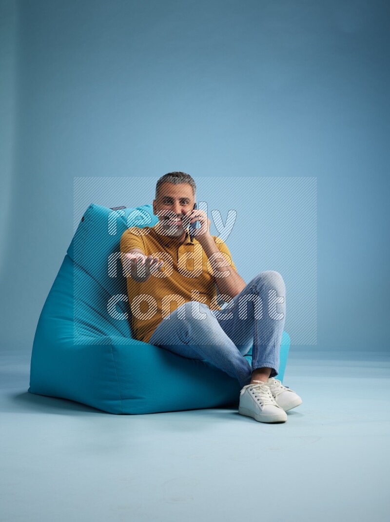 A man sitting on a blue beanbag and talking on the phone