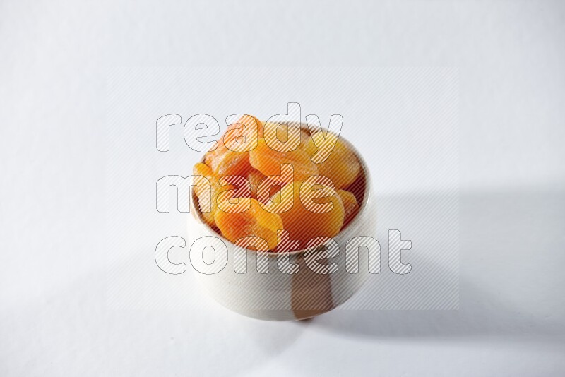 A beige ceramic bowl full of dried apricots on a white background in different angles