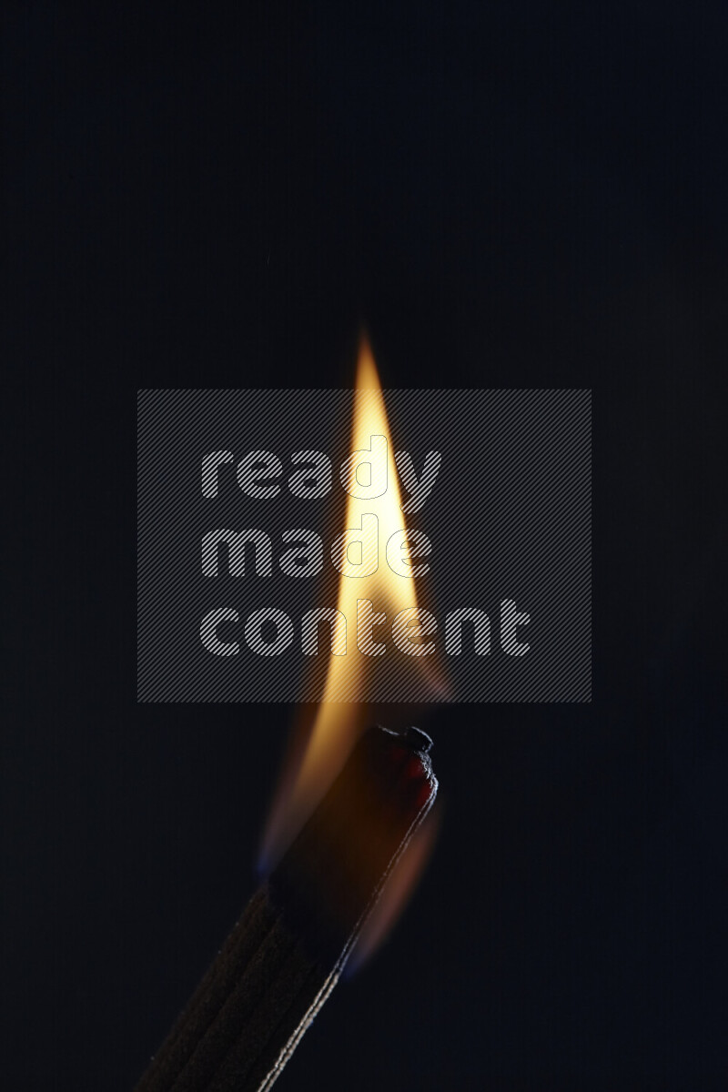 A burning incense stick isolated on dark backdrop