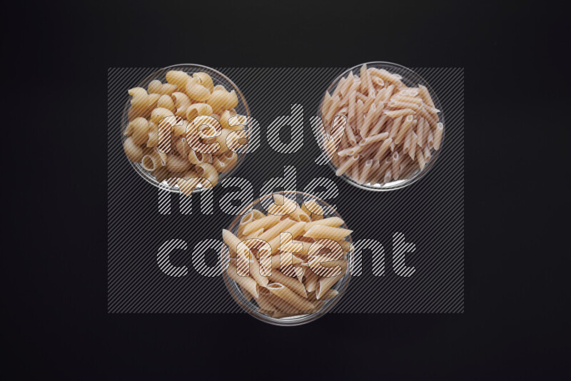 Different pasta types in glass bowls on black background