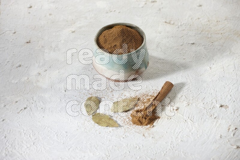 Cinnamon powder in a ceramic bowl with cinnamon sticks and laurel leaves on white background