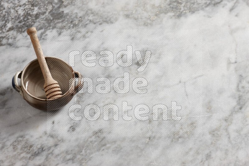 Multicolored pottery bowl with wooden honey dipper in it on grey marble background