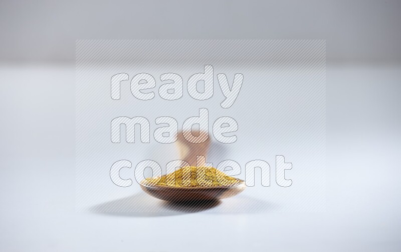 A wooden ladle full of turmeric powder on white flooring
