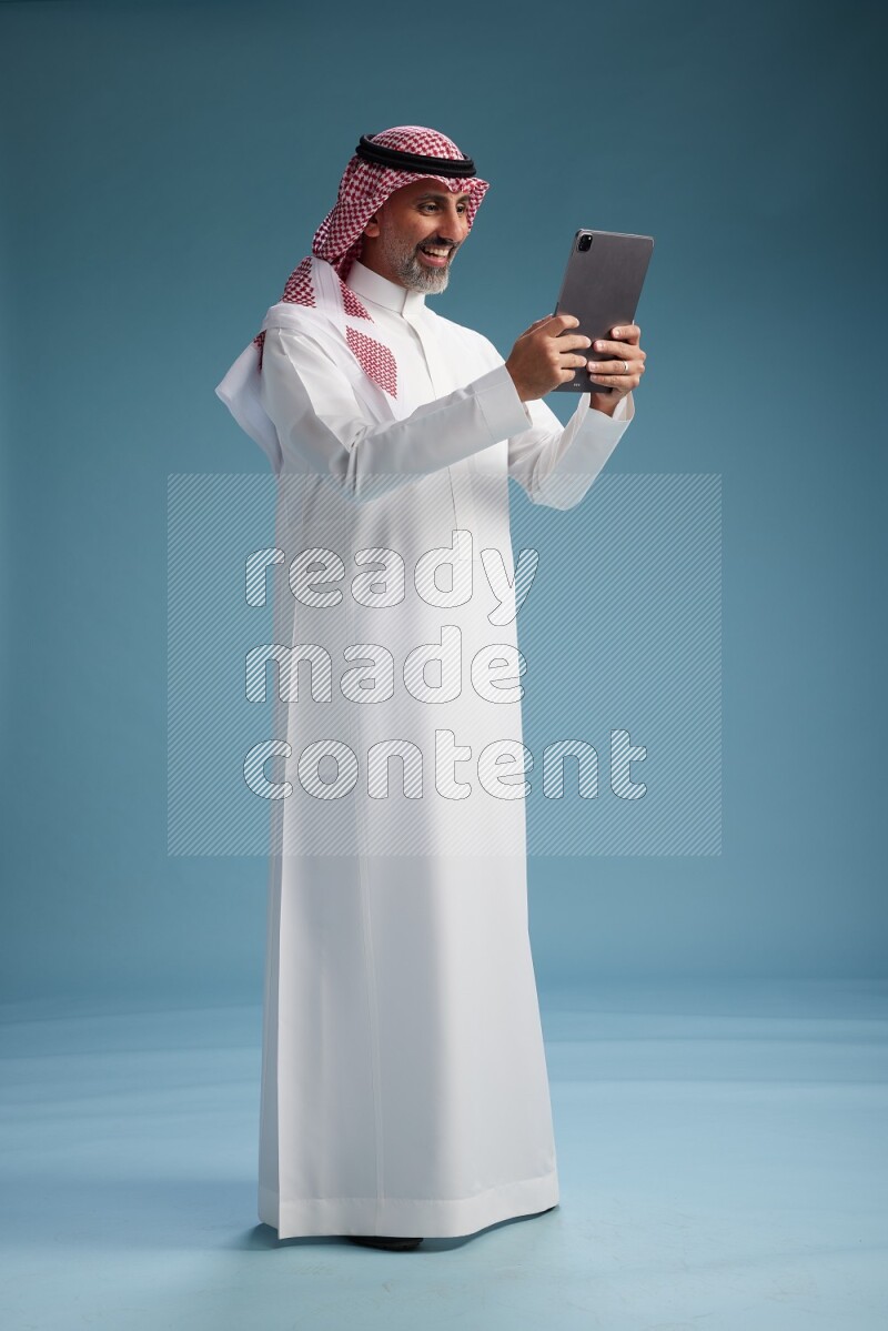 Saudi man wearing thob and shomagh with tablet on Blue background