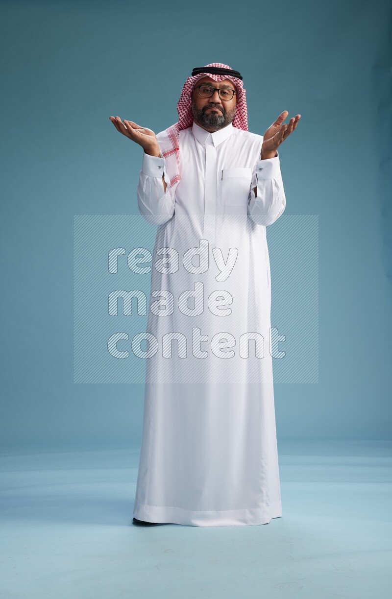 Saudi Man with shimag Standing Interacting with the camera on blue background