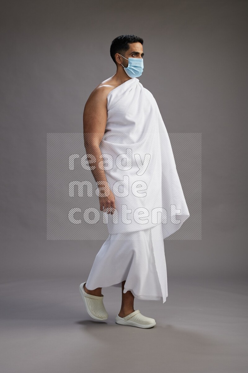 A man wearing Ehram with face mask Standing Interacting with the camera on gray background