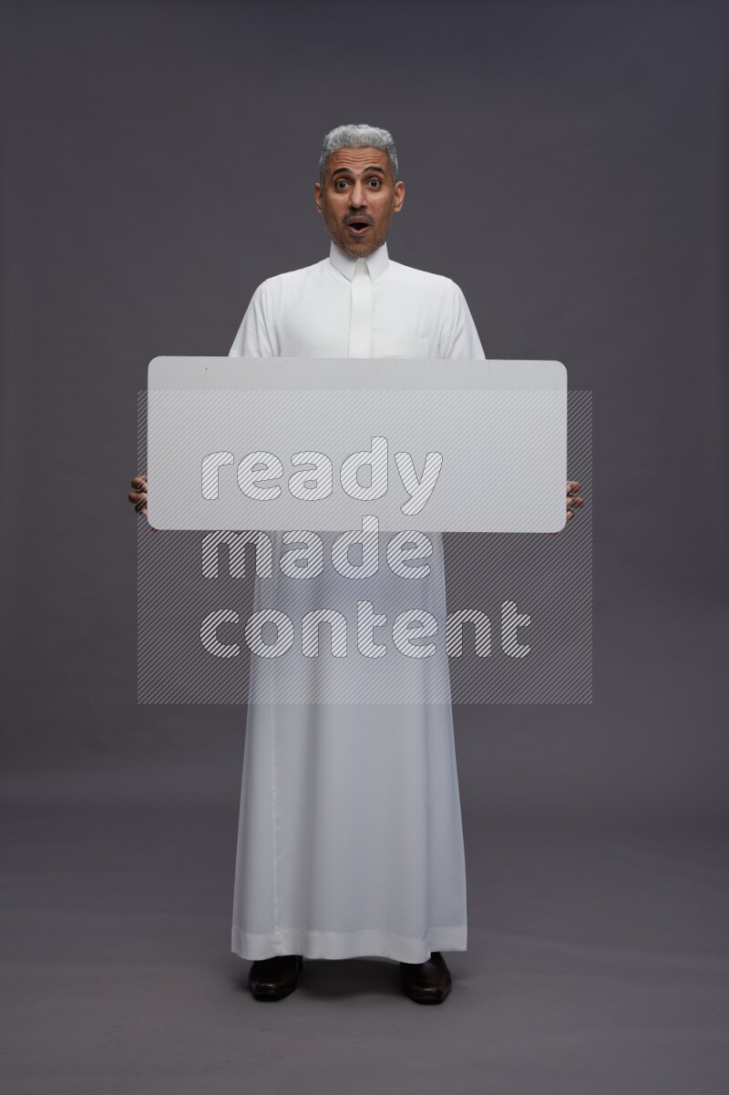 Saudi man wearing thob standing holding board on gray background