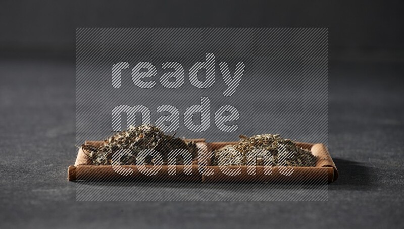 2 squares of cinnamon sticks full of cumin and dried basil on black flooring