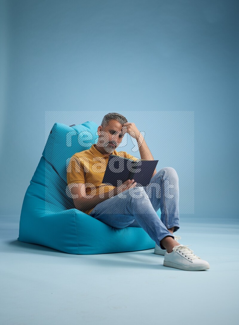 A man sitting on a blue beanbag and reading a book