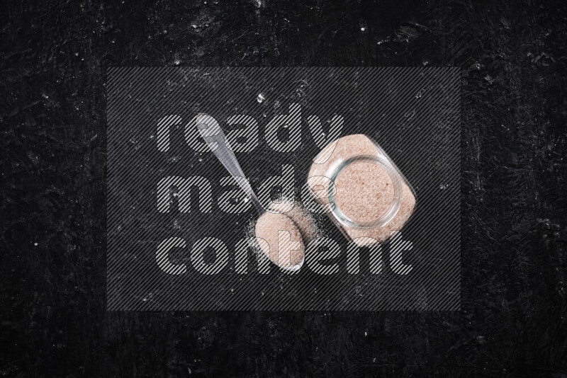 A glass jar full of fine himalayan salt on black background
