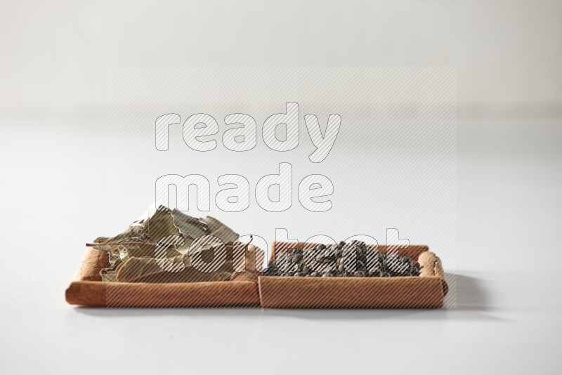 مربعان من أعواد القرفة ممتلئان بحبوب الفلفل الأسود وأوراق الغار علي خلفية بيضاء