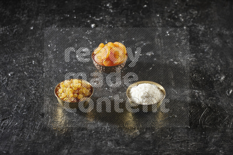 Dried fruits in metal bowls in a dark setup