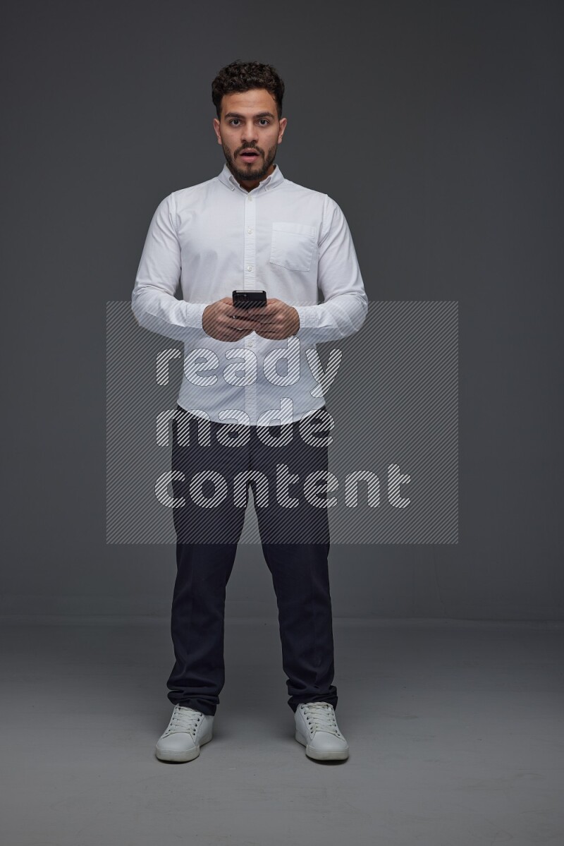 A man wearing smart casual standing and using his phone eye level on a gray background