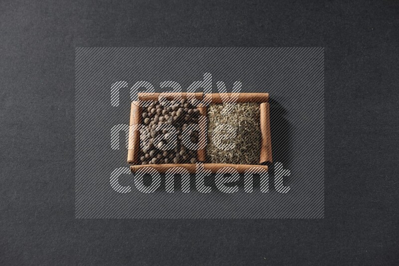 مربعان من أعواد القرفة ممتلئان بحبوب الكمون وحبوب بهار الفلفل الحلو علي خلفية سوداء