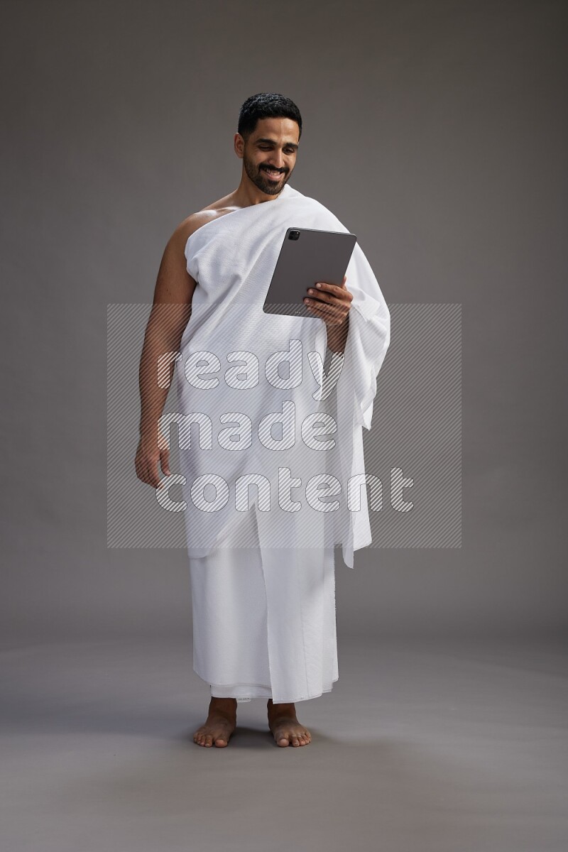 A man wearing Ehram and holding a tablet on gray background