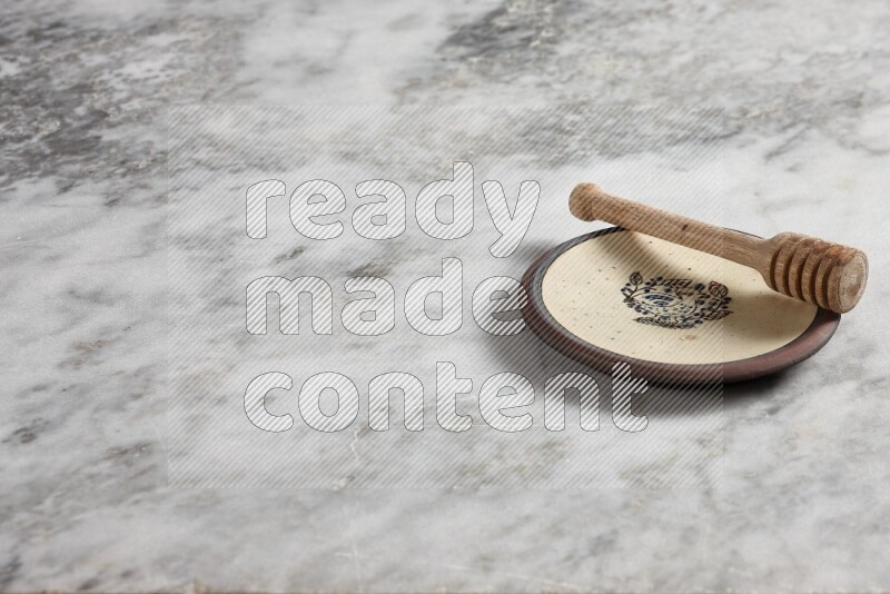 Decorative pottery plate with wooden honey dipper in it on grey marble background