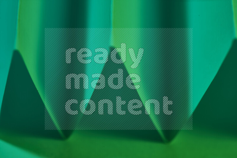 A close-up abstract image showing sharp geometric paper folds in green gradients