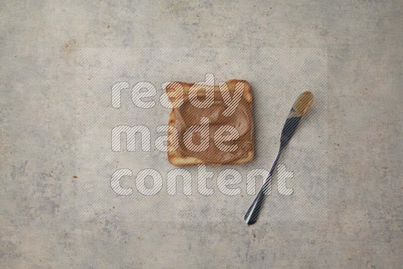 Creamy peanut butter on a toasted white toast slices with a spreading knife on a light blue textured background