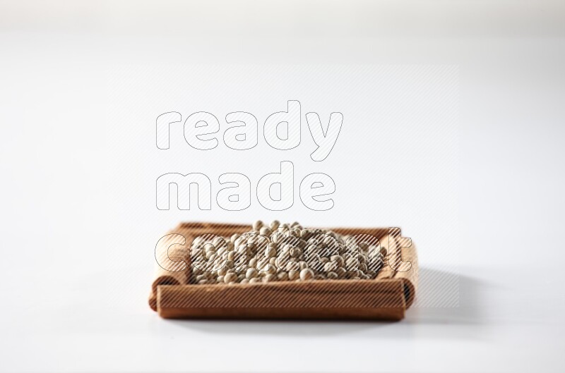A single square of cinnamon sticks full of white pepper on white flooring