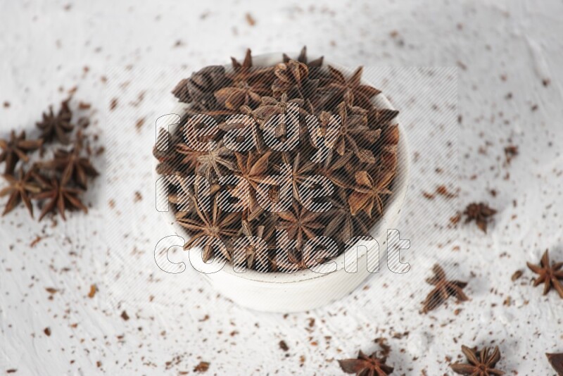 Star Anise in a white bowl and more of it sprinkled on white background