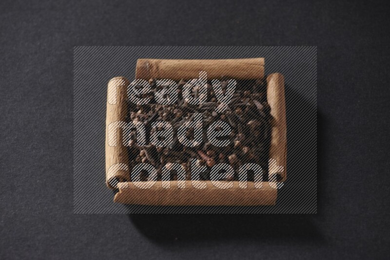 A single square of cinnamon sticks full of cloves on black flooring