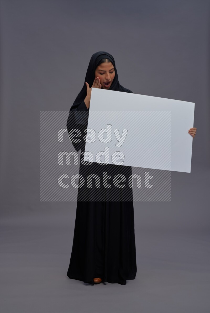 Saudi woman wearing Abaya standing holding white board on gray background