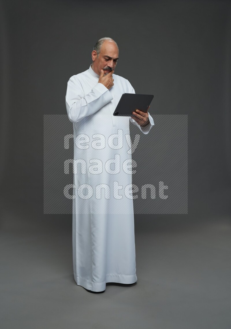 Saudi man without shomag Standing working on tablet on gray background