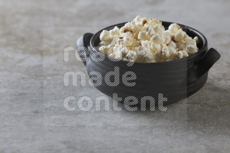 popcorn in a black handheld ceramic bowl on a grey textured countertop