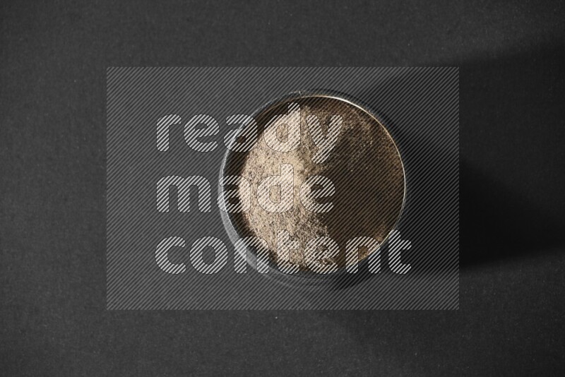 A black pottery bowl full of black pepper powder on black flooring