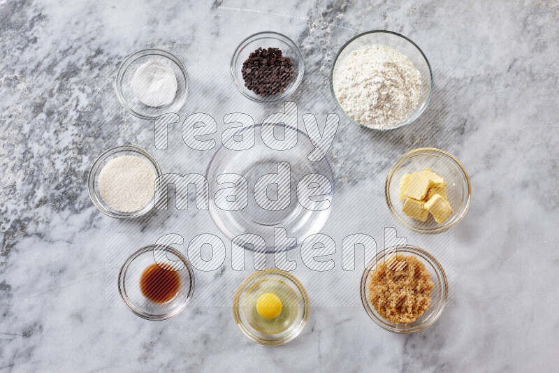 Cookies step by step with its ingredient, flour, butter, brown sugar, egg, vanilla extract, white sugar, chocolate chips and baking soda on grey marble background