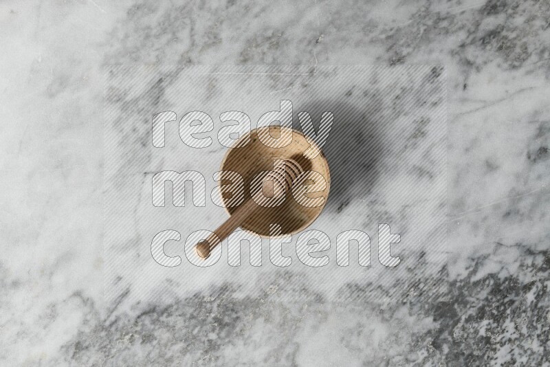 Beige pottery bowl with wooden honey dipper in it on grey marble background