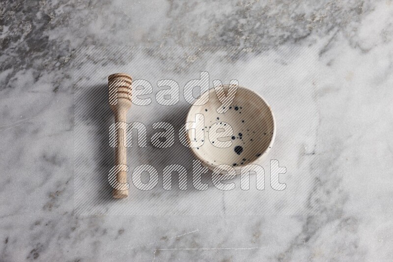 Multicolored pottery bowl with wooden honey dipper on the side on grey marble background